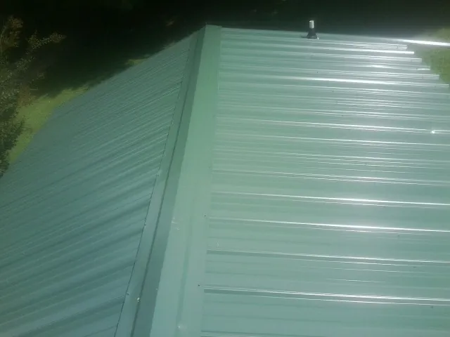 New green metal panels meeting at the ridge of a roof — Flat Roof Repair work by our crew in Laurens