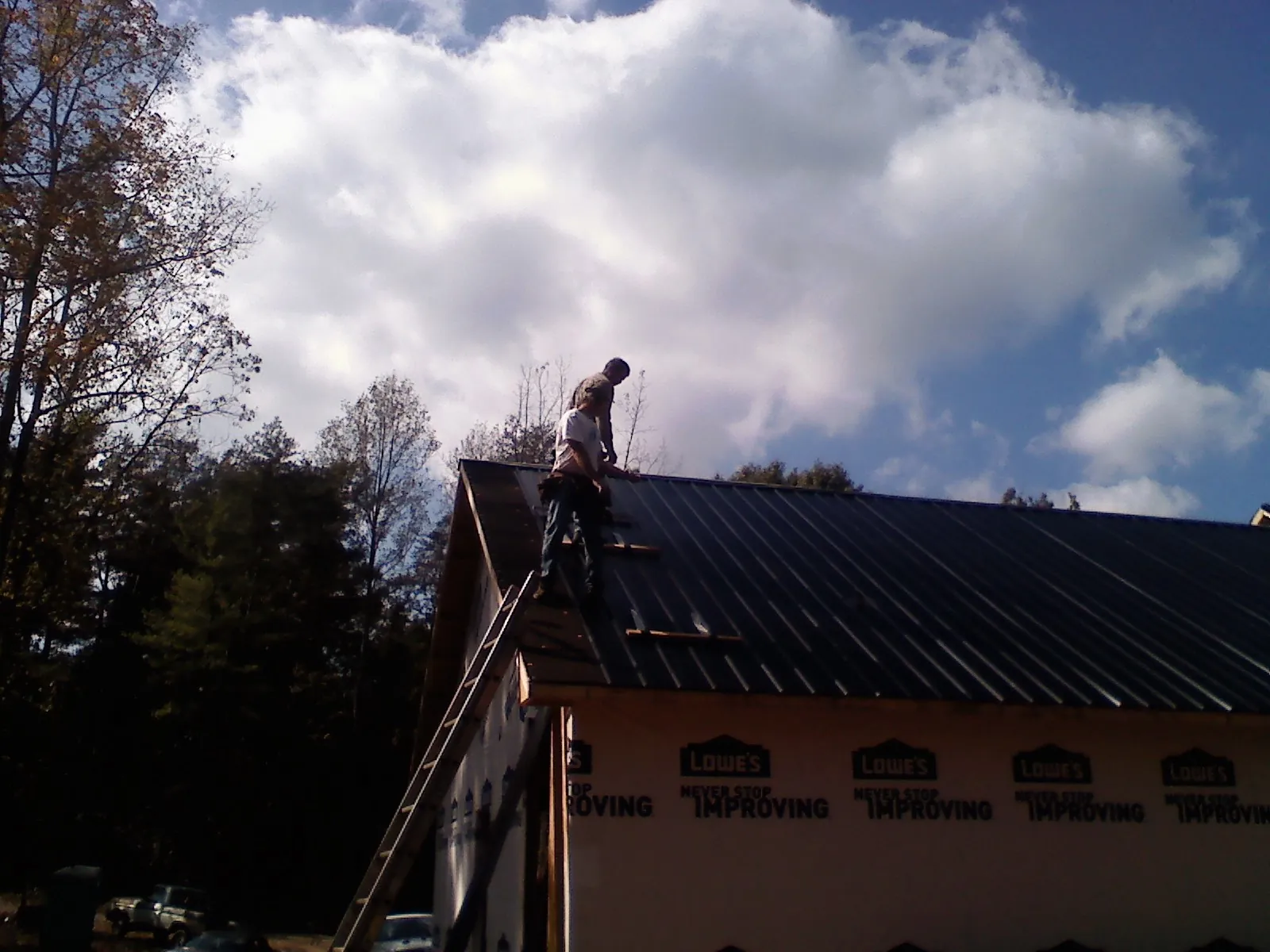 Roofer fastening dark metal panels high against a cloudy sky, from a Roof Inspection job in Laurens