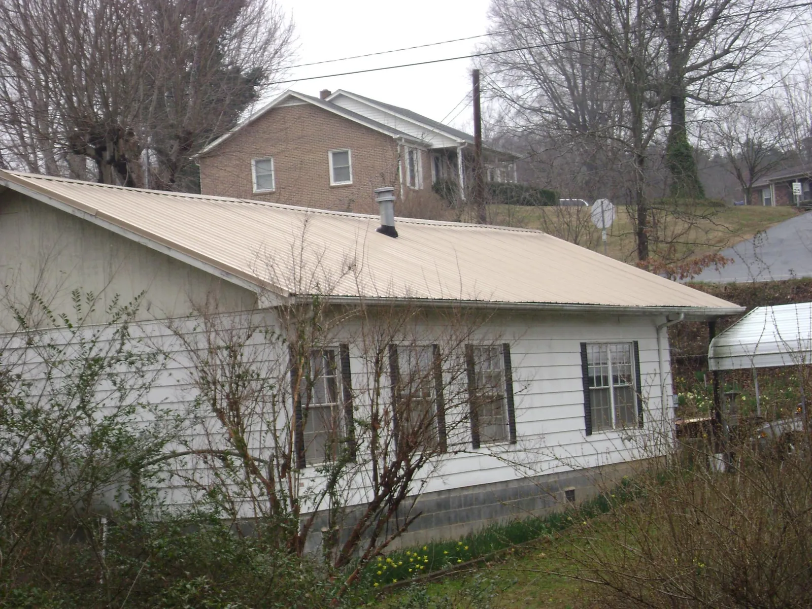 Tan metal roof on a white sided house set into a hillside — Commercial Roofing by Roofing Brothers in Laurens