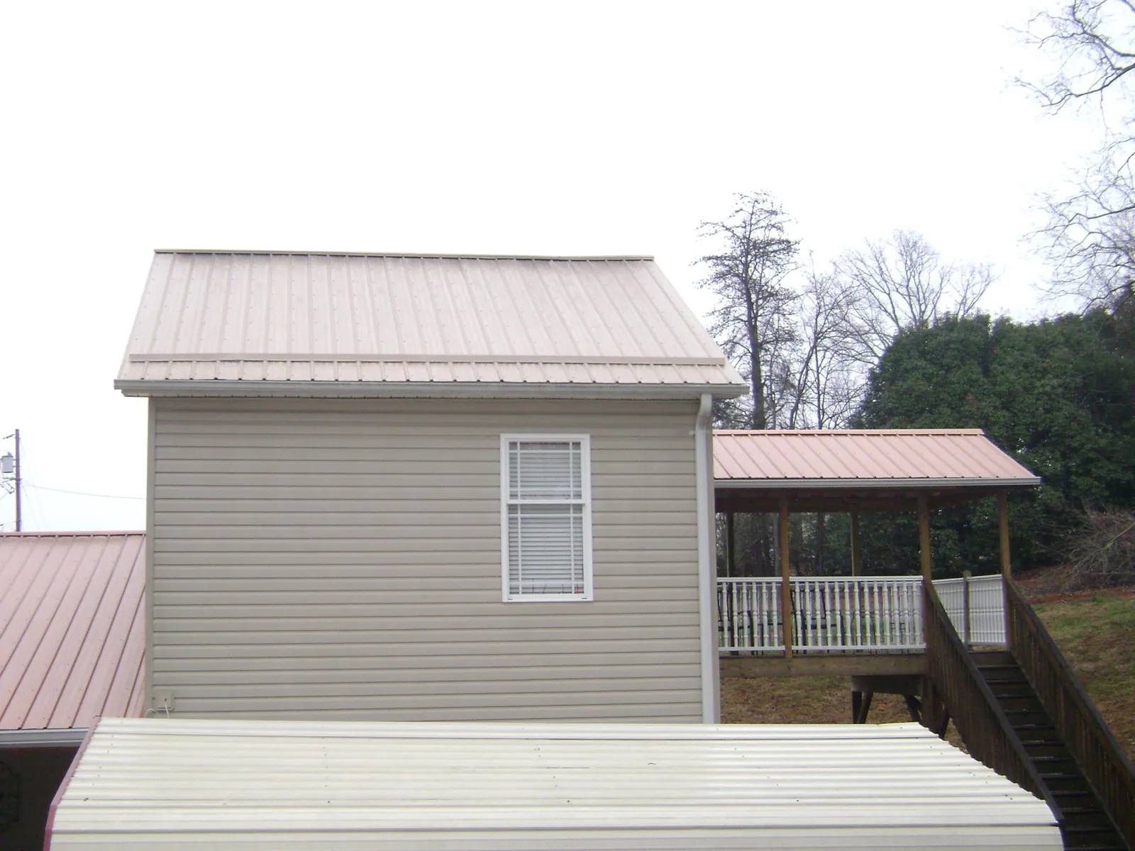 Tan metal roofs on a two story addition and attached porch, from a Roof Replacement job in Laurens